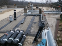 Foto van een plat dak waarop nieuwe rollen bitumen klaarliggen voor montage.